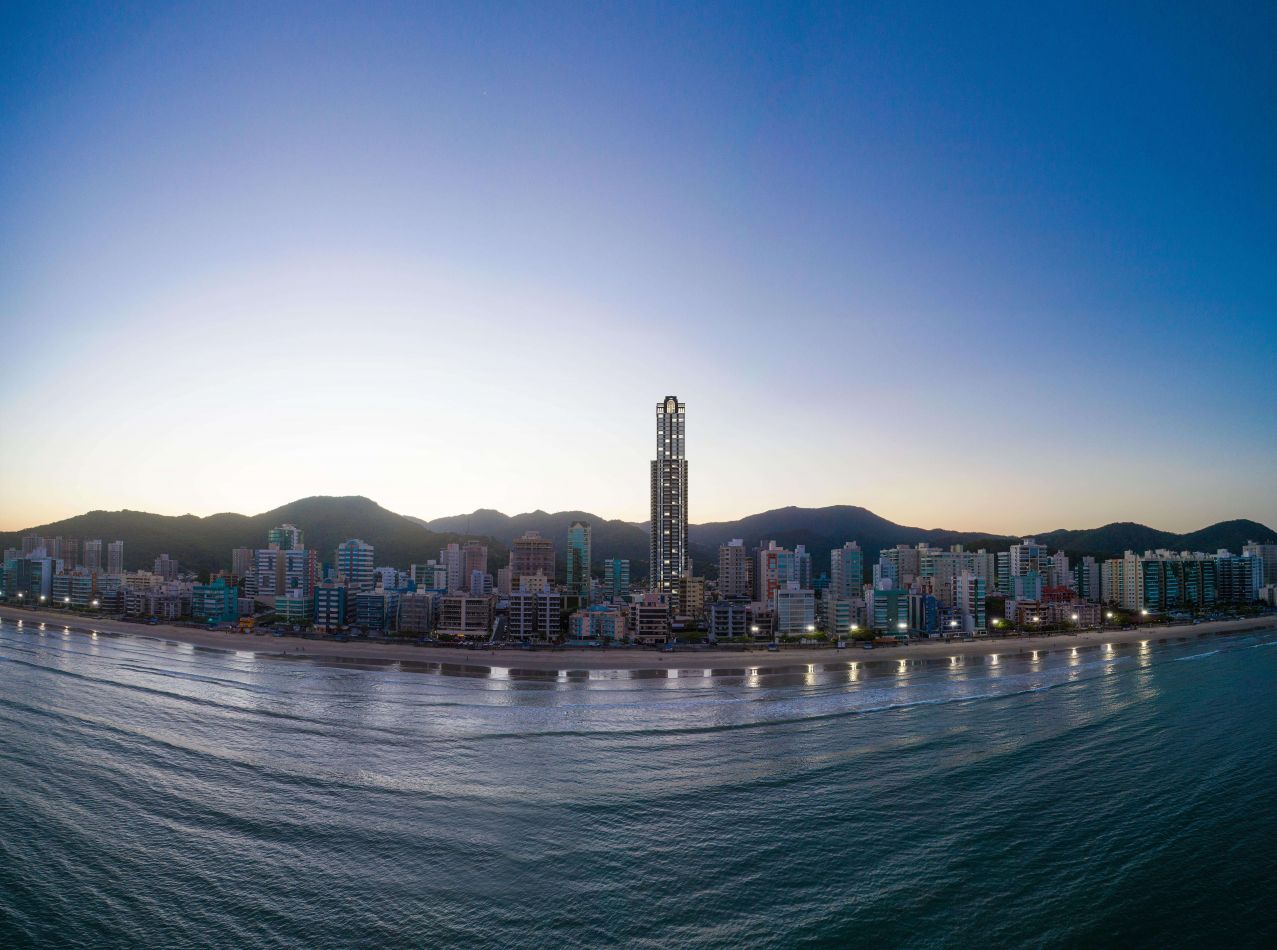 Vista aérea panorâmica do litoral de Itapema ao entardecer, com a torre do La Rocca no horizonte